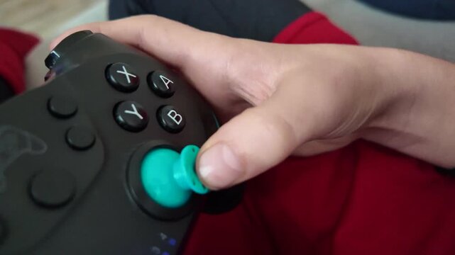 A child's hand moves quickly on a video game controller, pressing buttons and joysticks. The child's face is not shown.