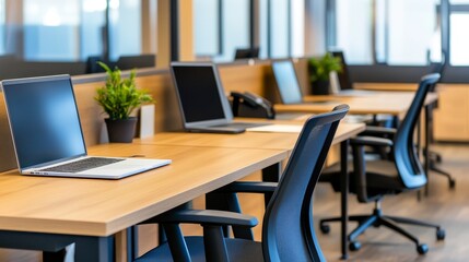 Modern office workspace with empty desks, laptops, and plants, showcasing a professional environment