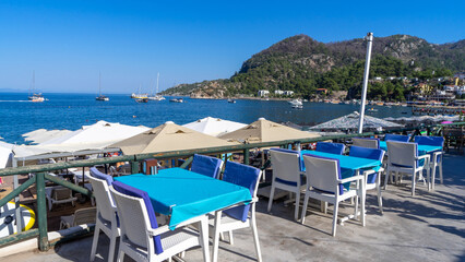 Street cafe with white chairs and blue tablecloths on Mediterranean Sea embankment in village of Turunc, Turkey. Vacation at resort. Eating outdoors