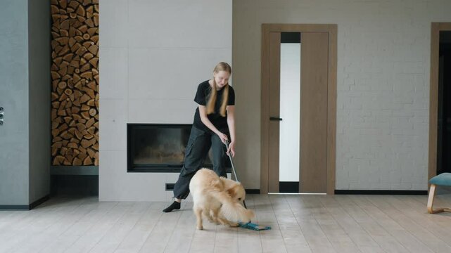Teenage girl playfully dancing with a mop while cleaning, as an energetic Golden Retriever joyfully runs around in a modern living room.