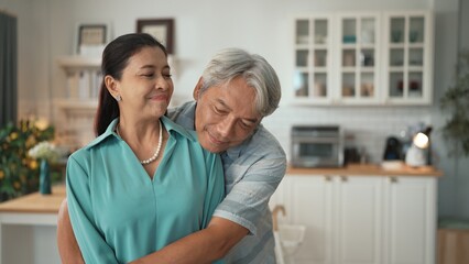 Fototapeta premium Happy senior couple with casual cloth spending time together and hugging at modern kitchen. Grandmother and grandfather holding hand together and looking at camera. Healthy relationship. Myrmidon.