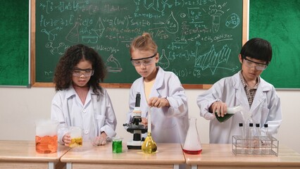 Children doing experiment in science lesson while standing at blackboard at laboratory. Happy student discovering and learning about biochemical liquid while inspecting and mixing sample. Pedagogy.
