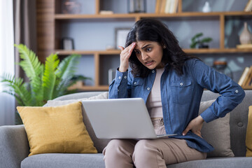 A young woman looks stressed while working on her laptop at home, showing a feeling of frustration.