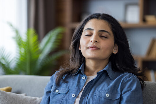 A serene woman finds peace and calm while practicing mindfulness meditation in her living room at home.
