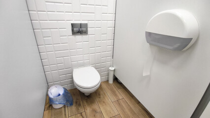Modern public restroom with a wall-mounted toilet, white geometric tiles, a toilet paper dispenser,...