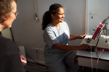 Smiling female medical professional operating machine while doing medical exam of senior patient in hospital