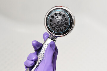 Hand in a rubber glove holds the shower head. Chrome-plated shower head with different shower modes