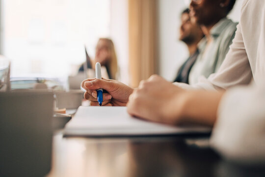 Hand of businesswoman writing with felt tip pen on book during meeting in office