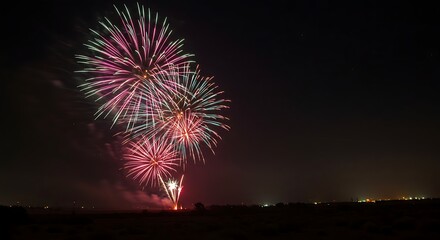 Fototapeta premium Colorful Fireworks Display Exploding in the Night Sky Over Dark Landscape