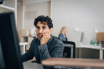Tired businessman leaning on elbows while using desktop PC in office
