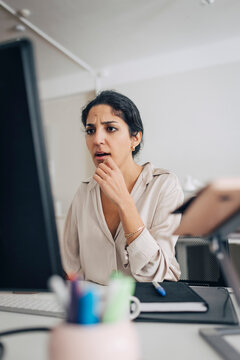 Confused female creative professional using desktop PC while sitting at desk in office