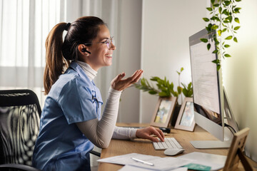 Smiling female doctor finishing paperwork and giving online advices on forum at home office.