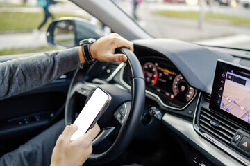 Cropped picture of a man's hands driving a car on a street and typing a message.