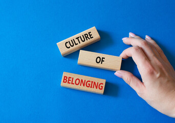 Culture of Belonging symbol. Wooden blocks with words Culture of Belonging. Businessman hand. Beautiful blue background. Business and Culture of Belonging concept. Copy space.