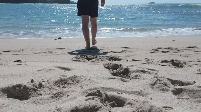Man walks towards sparkling ocean leaving footprints in the sand