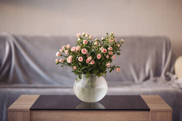 Beautiful bouquet of pink roses in a glass vase on a wooden table in a cozy living room setting