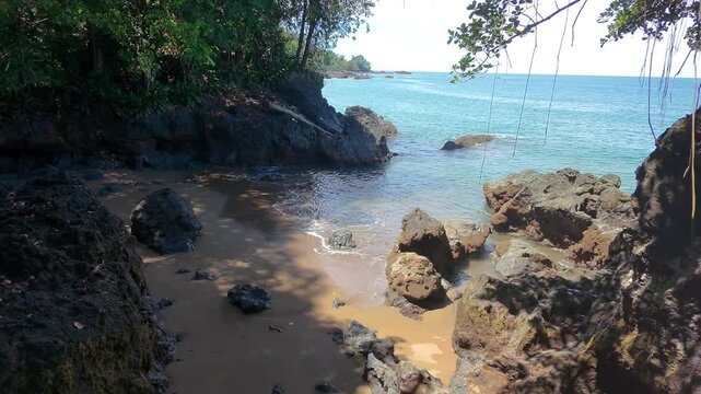 Flying back over a beautiful cove in Costa Rica revealing rocks and the rainforest jungle. Blue ocean and sunhine.