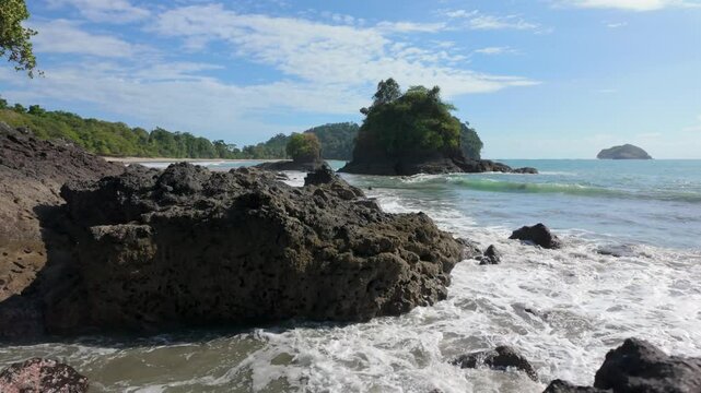 Camera tracks forwards moving past foreground rocks revealing the beautiful blue ocean of Manuel Antonio beach