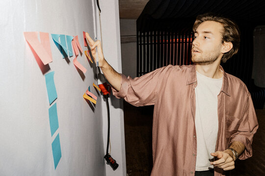 Young male entrepreneur sticking adhesive notes on wall during meeting at office