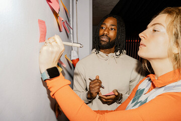 Female entrepreneur writing on adhesive notes while standing with colleague at office