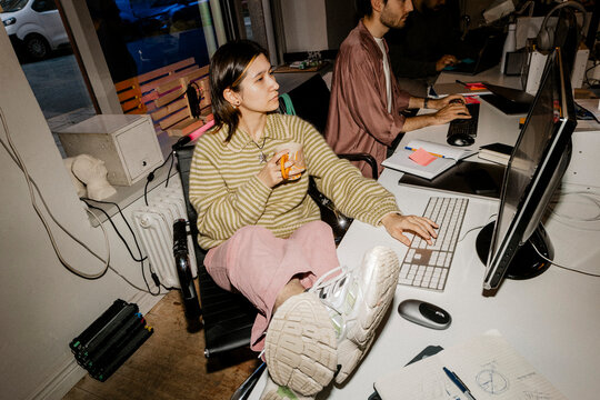 High angle view of female entrepreneur using computer while sitting with feet up on desk at office