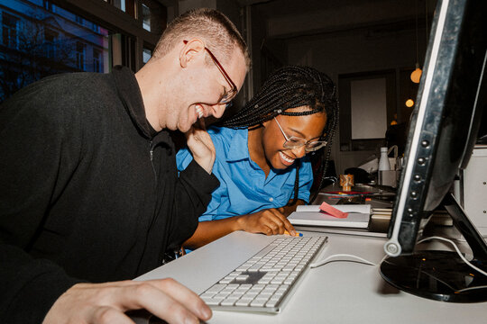 Happy multiracial male and female business professionals sitting at desk in office