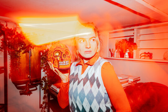 Businesswoman holding artificial human skull and looking away amidst bright orange lights