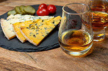 Whiskey and cheese pairing, tasting whisky glasses and plate with sliced crumbly old blue stilton and blue shropshire cheeses, Great Britain food and drink