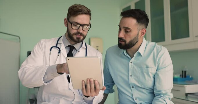 Serious Caucasian doctor showing medical check-up result to male Latin patient, using tablet computer, explaining online electronic report, treatment recommendation