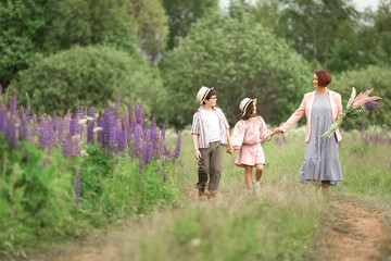 Fototapeta premium Caucasian family stroll: mother with son and daughter in nature holding flowers