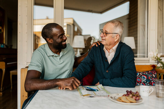 Happy male caretaker talking with senior man while giving emotional support