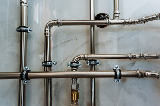 Sleek stainless steel pipes against a resilient wall create a stunning visual display with their shine and modern design, ideal for plumbing and construction applications