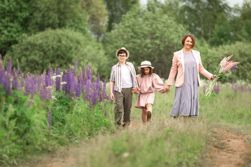 Fototapeta premium Mother with children walking in meadow holding flowers