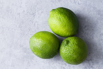 Fresh green limes on a gray concrete surface. Vibrant citrus fruit for tropical recipes. Empty copy space fruit background. Healthy drinks and organic ingredient use.