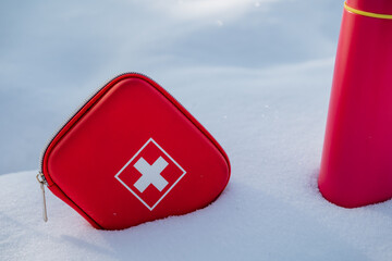 A bright red first aid kit prominently stands out in the snowy landscape next to a cheerful pink...
