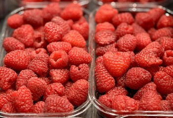 Fresh red raspberries in a transparent container for sale on the supermarket counter. A delicious ripe berry for a healthy diet. Close-up