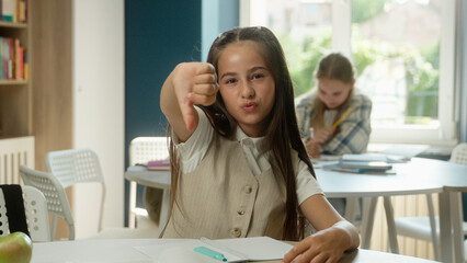 Obraz premium Caucasian girl teen schoolgirl pupil learner student daughter child kid primary school education lesson task writing exam dissatisfied thumb down gesture finger dislike bad studying learning library