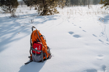 A backpack, colored and sturdy, is resting in the soft, white snow right beside an essential first...