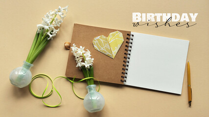 Open notebook with blank pages, heart-shaped paper cutout, white flowers in vases, and Birthday...