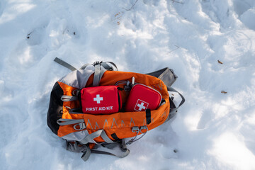 Amidst deep, shimmering snow, a large backpack full of first aid kits sits silently, surrounded by...