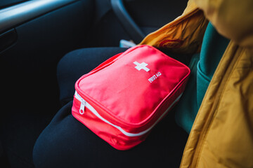 A person is comfortably sitting in a car with a first aid kit resting in their lap, ready for any...