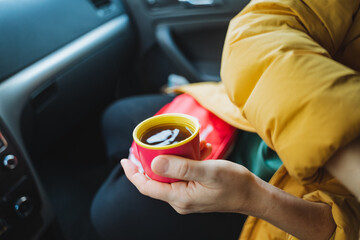 A person is seated comfortably in the drivers seat of a car, savoring a warm cup of coffee while...