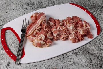 Cut up bacon slices on a white cutting board with a fork
