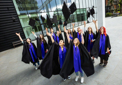 Group of young students throws their graduation hats in the air.