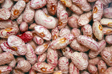 A collection of wrinkled, pink and cream colored beans. Their varying shades and textures suggest natural irregularities,creating an intricate visual pattern.Pinto beans soaked in water, ready to eat.