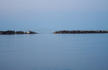 blue sea and blue sky before a storm, silhouette breakwater, sky and sea have the same color, gray blue clouds, evening sky,  gentle waves, reflection blue sky
