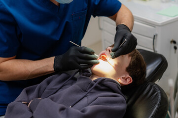 A dentist checks the teeth of a child who is sitting in an armchair with his mouth wide open. Routine dental check-up. Health