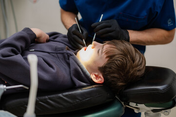 A dentist checks the teeth of a child who is sitting in an armchair with his mouth wide open....