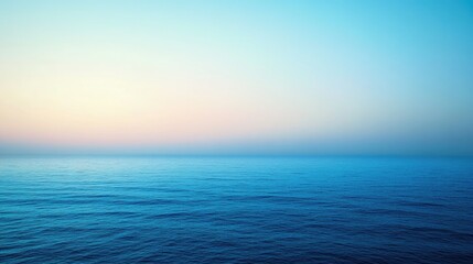 Panoramic view of the ocean during sunset. The sky transitions from blue to orange, blurring into the horizon. Clouds are visible above the water's surface, creating a serene and vast landscape.