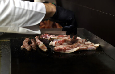 chef friendo a la plancha carne de panceta de cerdo con guantes en sus manos